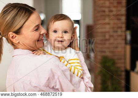 Maternal Love. Mother Holding Cute Infant Girl On Hands And Cudding, Embracing Baby And Smiling, Bed