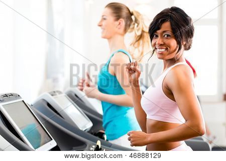 Running on treadmill in gym or fitness club - two women exercising to gain more fitness