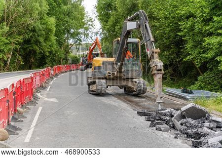 Excavator With Hydraulic Jack Hammer  Breaking Asphalt In Preparation For Drainage Works Close Up An