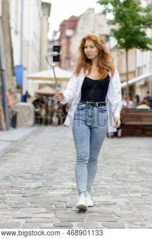 Young Redheaded Beautiful Woman Walking And Using Her Mobile Phone
