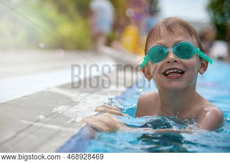 Happy Little Boy Swims In Clear Water In A Summer Outdoor Pool Wearing Swimming Goggles. Smiling Chi