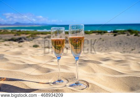 Two Glasses Of Rose Champagne Or Cava Sparkling Wine Served On White Sandy Tropical Beach With Dunes