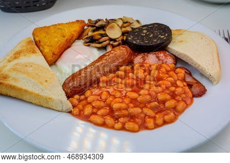 White Board With Full English Breakfast With Bacon, Fried Egg, Beans, Tomato, Roasted Sausage, Black