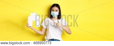Covid-19, Pandemic And Real Estate Concept. Cheerful Asian Woman Smiling In Medical Mask, Showing Pa