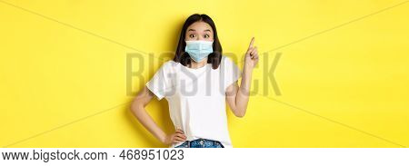 Covid, Health Care And Pandemic Concept. Asian Female Model In Medical Mask And White T-shirt Pointi