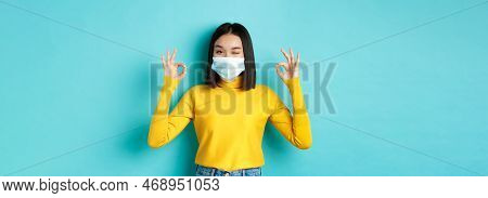 Covid-19, Social Distancing And Pandemic Concept. Cheerful Asian Girl In Medical Mask Showing Okay G