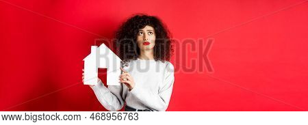 Real Estate. Sad Woman Thinking Of Buying Own House, Showing Paper Home Cutout And Looking Up With U