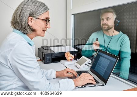 Experienced Female Audiologist Doing Hearing Test To Male Patient In Soundproof Audiometric Booth Wi