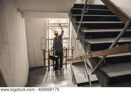 A Worker With Toolbox In Hands Looking Trough The Window In A Building At Construction Process.