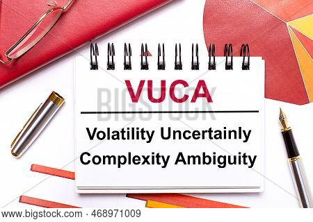On The Desktop Is A White Notebook With The Text Vuca Volatility Uncertainly Complexity Ambiguity, A
