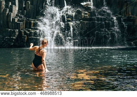 Caucasian Woman In Black Swimsuit Entering Into Waterfall Lake Surrounded Black Volcanic Stone Washe