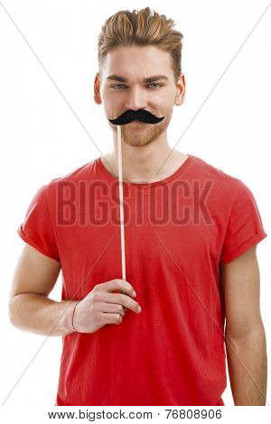 Handsome young man holding a fake moustache in front of his hace