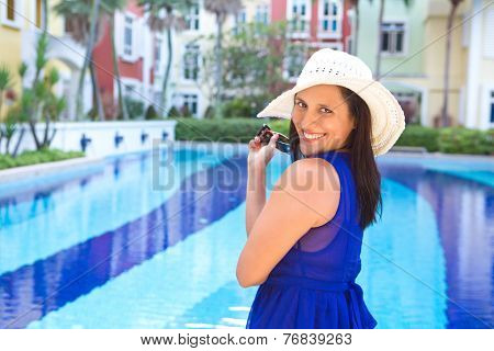 Beautiful woman in blue dress and white hat smiling by the swimming pool
