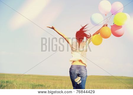 young asian woman running and jumping on green grassland with colored balloons