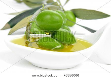 closeup of a twig of olive tree with olives on a bowl with olive oil