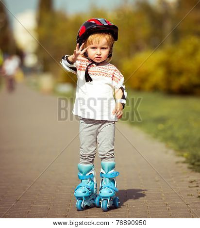 two year old pretty girl in roller skates and a helmet on the street