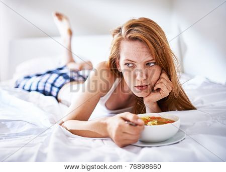 woman in bed eating chicken noodle soup while sick