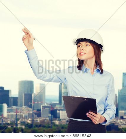 building, developing, consrtuction and architecture concept - smiling businesswoman in white helmet with clipboard pointing finger