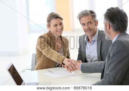Couple in bank office shaking hand to financial adviser