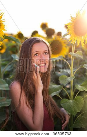 Young girl talking on the phone on among sunflowers at sunset