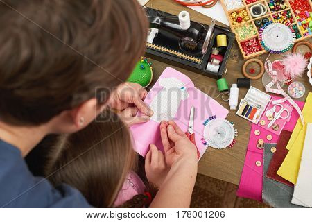 mother teaching daughter to sew doll clothes, top view, sewing accessories top view, seamstress workplace, many object for needlework, handmade and handicraft