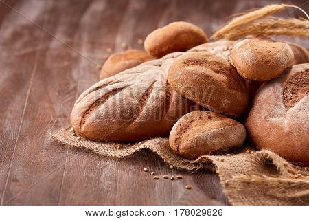 handmade tasty bread lying on burlap on the wooden table with flour, wheat and ears of wheat. Brown bread and rulls. Delicious food. Fresh baking. Tasty and appetizing.