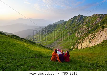 Three friend sit among the lawn looking upon a map and landscapes around scenes deciding the path of their trip.