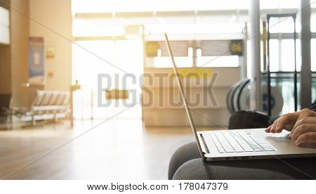 a man with a silver laptop and bag is waiting for for boarding near terminal working at the airport near the big window on sunny summer day