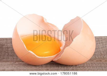 Broken egg with yolk and eggshell on a wooden table with a white background.