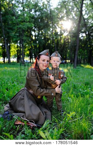 A small son with his mother in the uniform of a Soviet soldier against the background of nature. May 9, Victory Day, World War II, family, peace, against fascism.