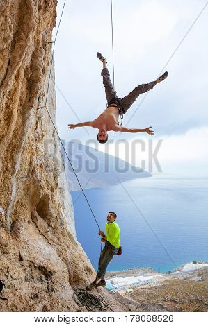 Rock climbers fooling around: one man hanging upside down while being lowered belayer watching him and smiling