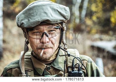 Norwegian Armed Forces Special Command FSK soldier smoking cigarette closeup portrait. Radio and headset are on