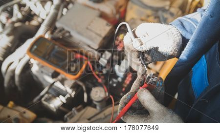Mechanic in auto workshop works with car electrics - electrical wiring, voltmeter - top view, close up