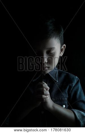 Little boy praying and praising God isolated on black.