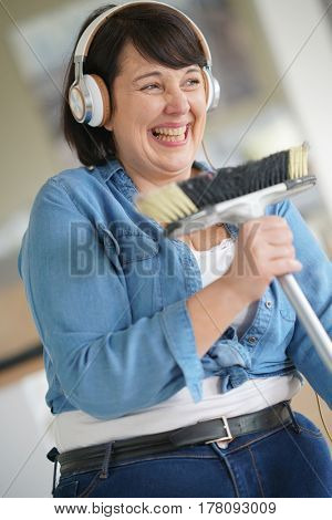Cheerful overweigth woman having fun sweeping the floor