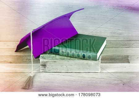 Graduation mortarboard on top of stack of books on the wooden table