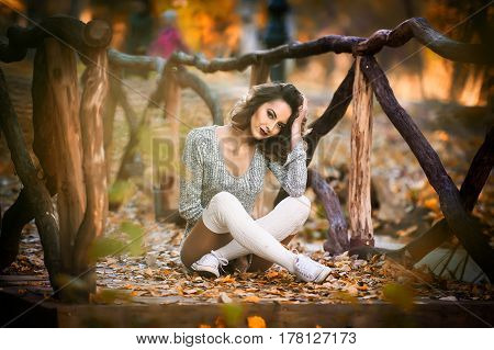 sensual girl with long legs laying down in an autumnal scene.Long legs attractive blonde with curly hair relaxing in autumnal park.Fashionable young woman posing in the forest.