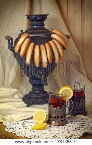 Russian samovar, tea with lemon in faceted glasses with cup holders and bublik. Tinted photo in vintage style.