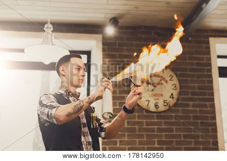 Hairdresser heating the blade of old-fashioned straight razor under stream of fire for smoother shaving. Stylish barber preparing tools for traditional beard shave at barbershop