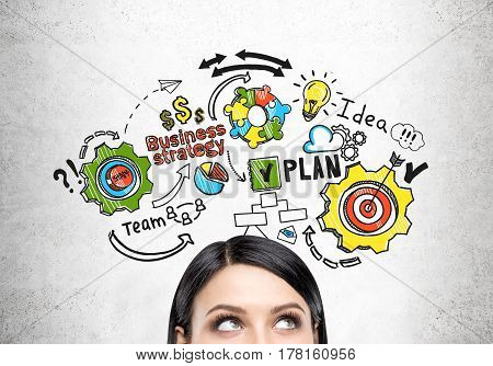 Close up of a head of a woman with black hair standing near a concrete wall with a colorful business plan drawing on it.