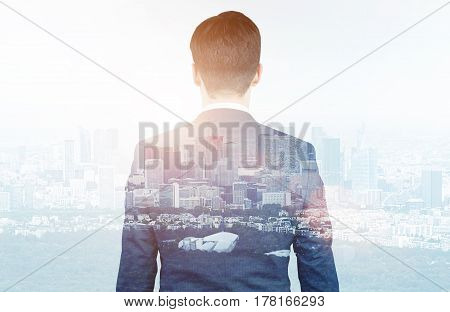 Rear view of a businessman wearing a suit and looking at a city panorma in the morning. Double exposure.