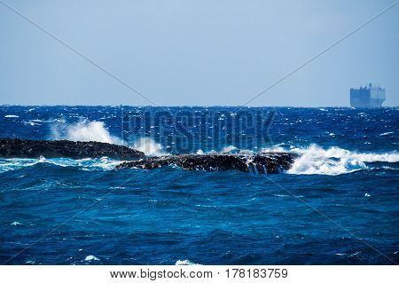 Big rocks in the middle of the water creating wave splashes and a boat far in the background. New Providence, Nassau, Bahamas.