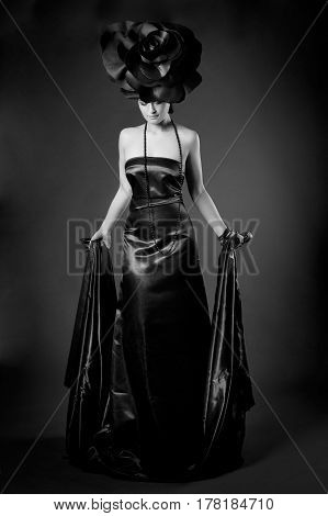 black and white Full-length dark portrait of a girl in a black dress and a rose hat.