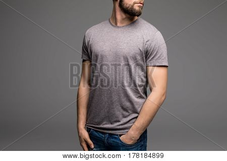 A Man In A Grey T-shirt And Denims Holds His Hands In Pockets.