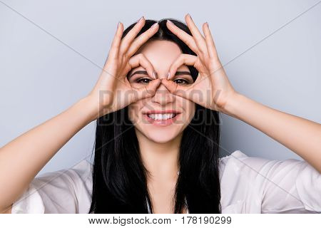 Young Cheerful Laughing Woman Having Fun And Making Binoculars Using Her Hands Isolated On Gray Back