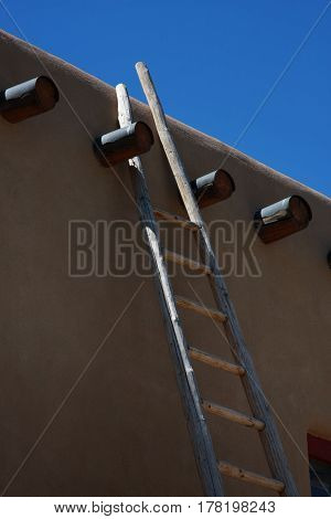 A wooden ladder is leaning against the wall of an adobe structure between two vigas in New Mexico