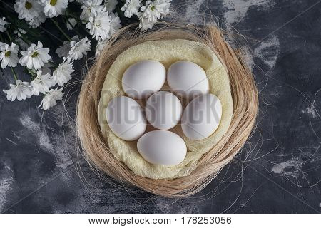 White Chicken Eggs In Easter Nest On Gray Background. Top View