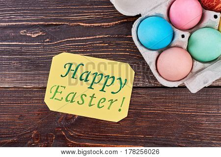 Easter card on brown wood. Bright eggs in a tray. Rustic easter ideas.