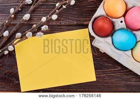 Easter eggs, blank yellow card. Willow branches on brown wood. Best ideas for Easter congratulations.