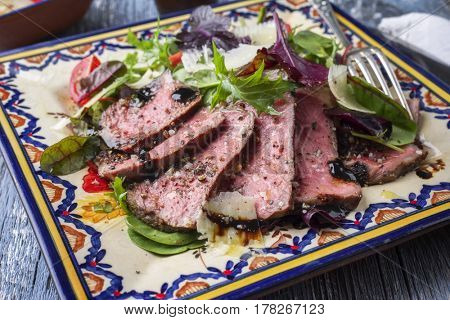 Traditional Italian Tagliata di Manzo Steak with Parmesan and Salad as close-up on a plate